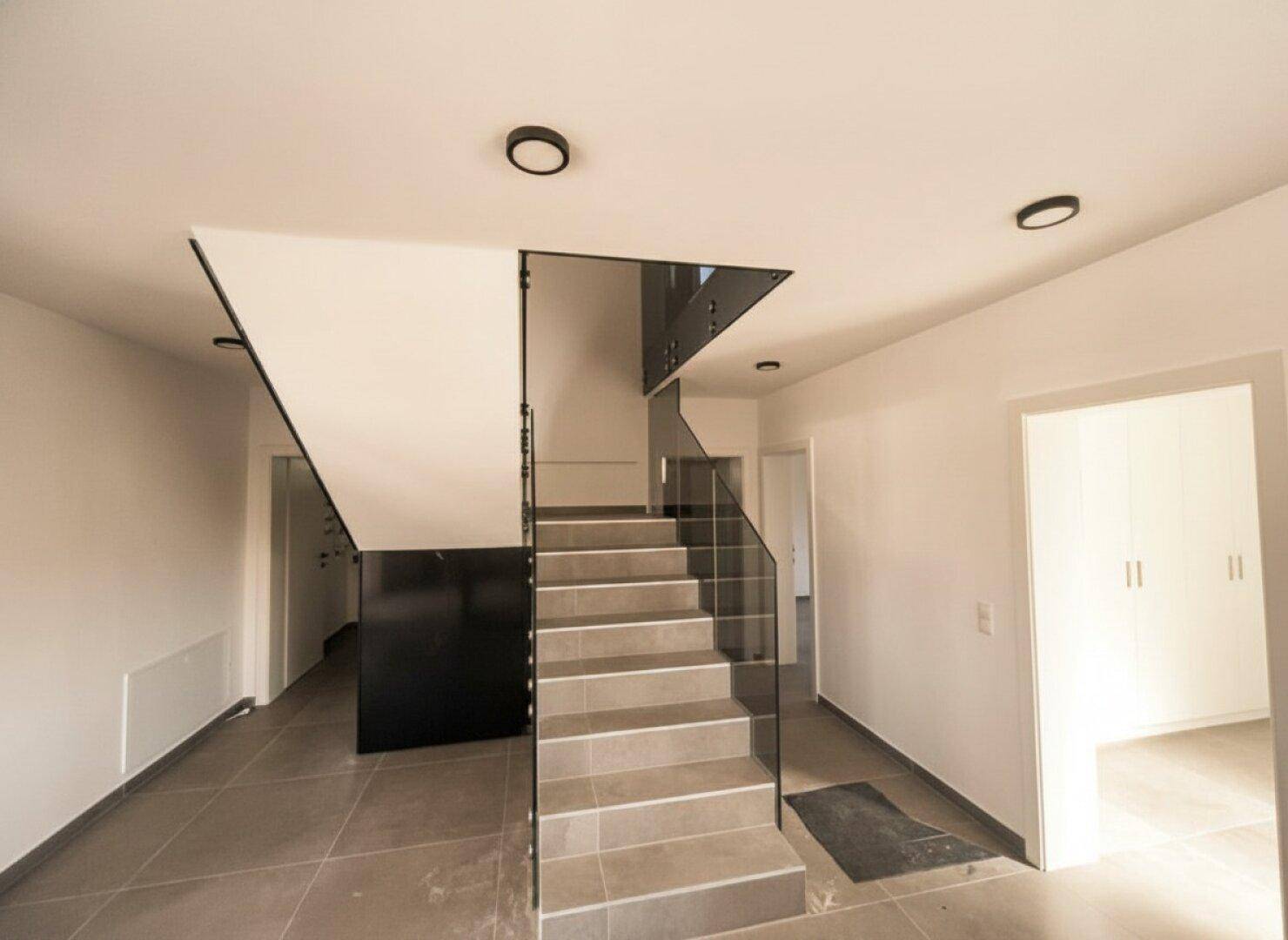Heller Eingangsbereich mit moderner Treppe aus Glas und Fliesenboden.