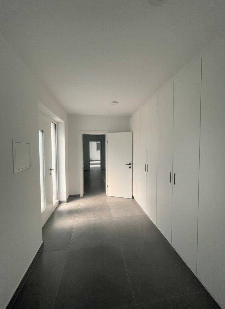 Langer, heller Flur mit integrierten weißen Einbauschränken und dunklem Fliesenboden.