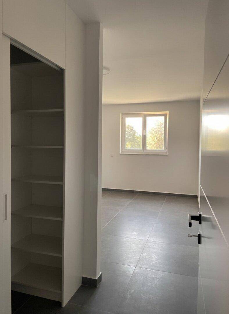 Helles Schlafzimmer mit Fenster und praktischem, offenem Regalbereich für Kleidung oder Lagerung.