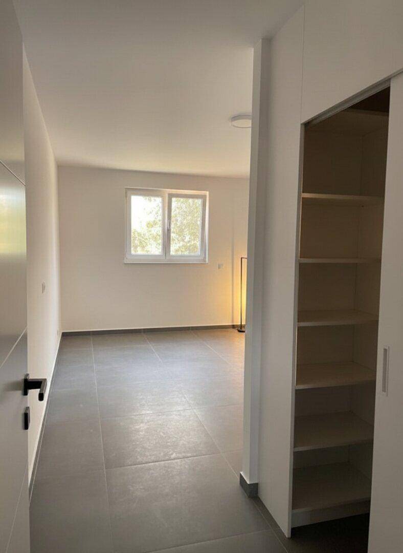 Geräumiges Schlafzimmer mit viel Tageslicht und integrierten Regalen, ideal für individuelle Gestaltung.