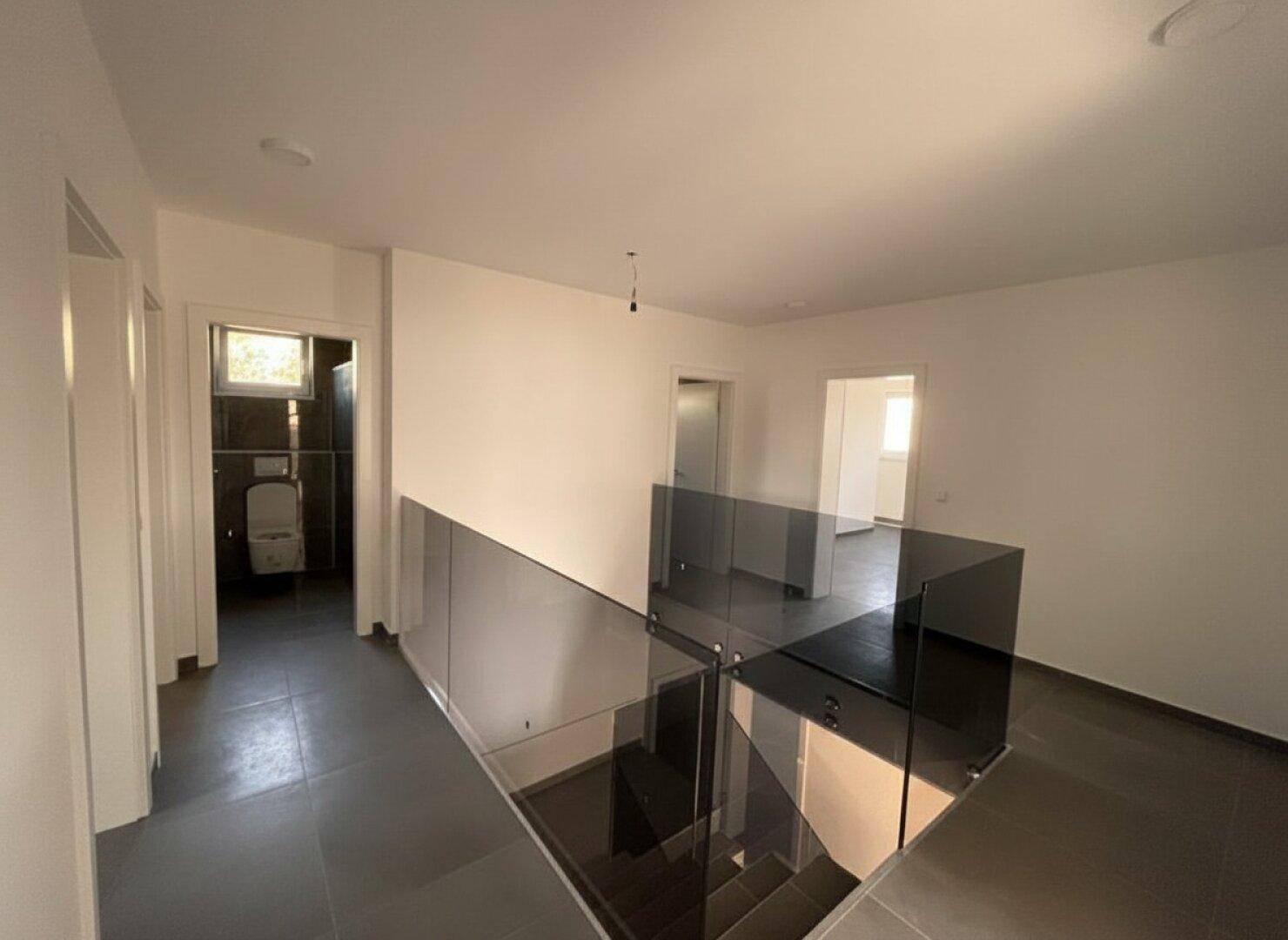 Heller Flur im Obergeschoss mit Glasgeländer und Blick in ein modernes Badezimmer.