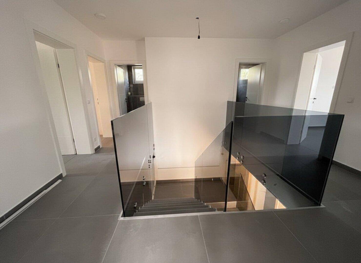 Moderner Treppenaufgang mit Glasgeländer, der die obere Etage mit dem Erdgeschoss verbindet.