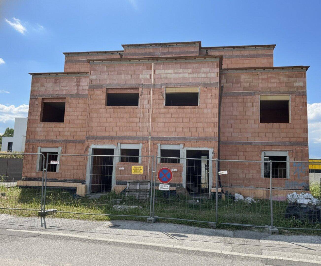 Vorderansicht des Rohbaus mit Bauzaun und zukünftigen Fenster- und Türausschnitten.