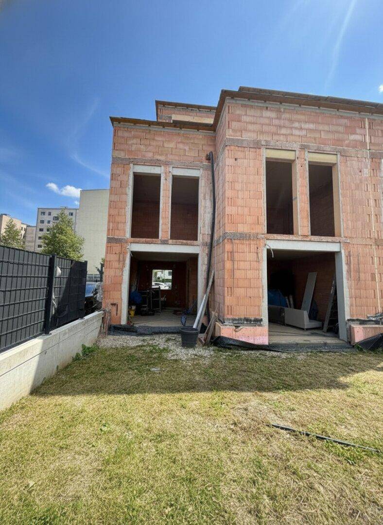 Rohbau eines Gebäudes mit großen Öffnungen für Fenster und Türen, umgeben von einer Rasenfläche.