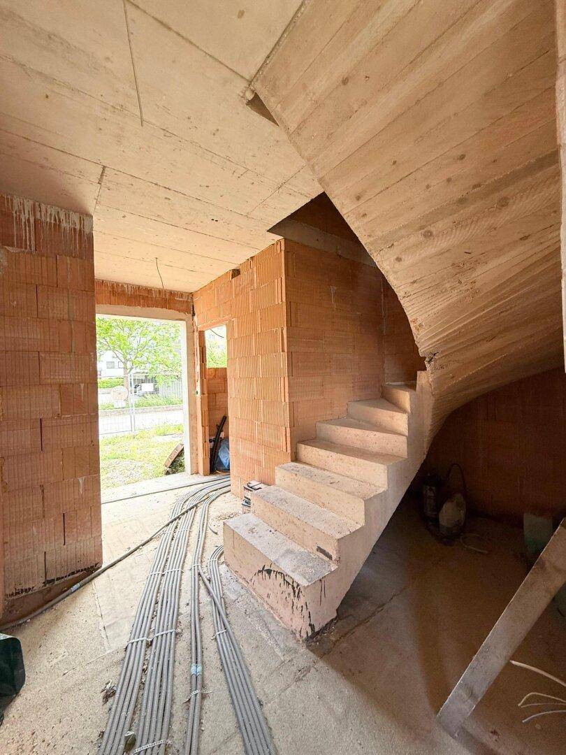 Unfertiges Treppenhaus im Rohbau mit sichtbaren Ziegelwänden und provisorischen Stufen.