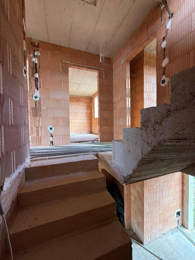 Treppenaufgang im Rohbau mit unverputzten Ziegelwänden und sichtbaren Elektroinstallationen.