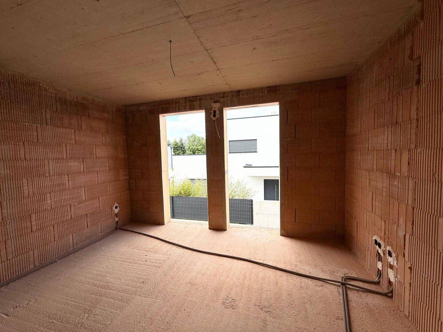 Schlafzimmer im Rohbau mit großen Fensteröffnungen und Blick auf die Nachbarbebauung.