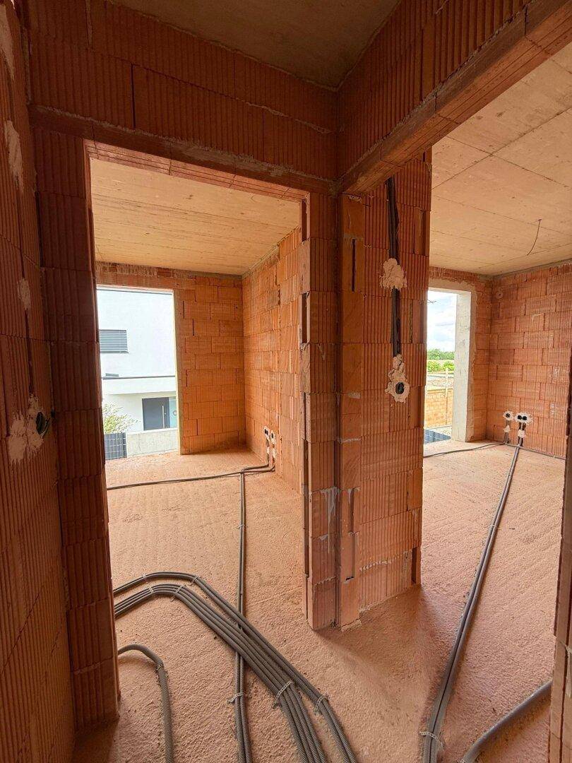 Geräumiger Raum im Rohbau mit großen Fensteröffnungen und vorbereiteten Leitungen für Installationen.