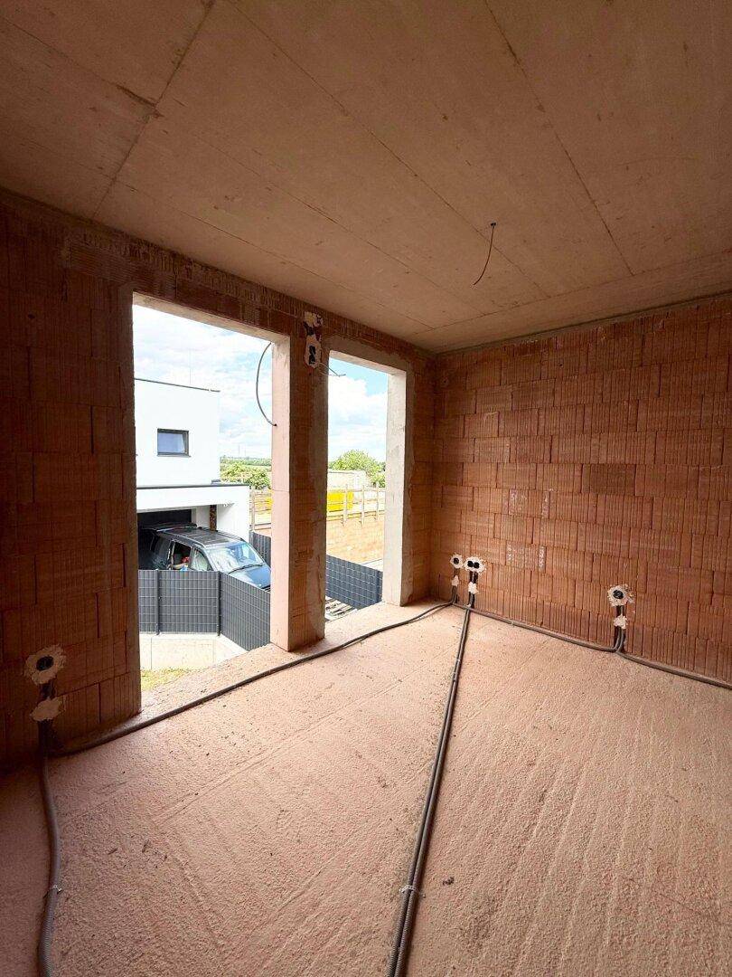 Zimmer im Rohbau mit großen Fensteröffnungen und Blick auf den Außenbereich.