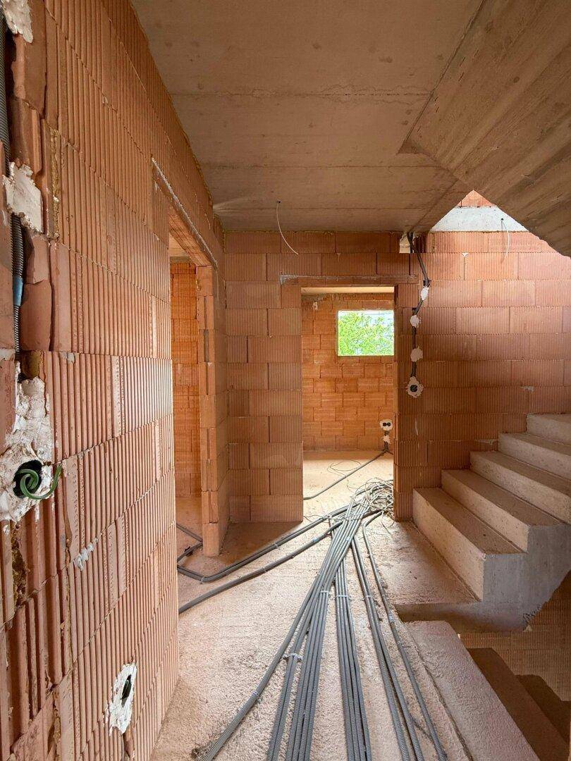 Flur und Treppenbereich im Rohbau mit sichtbaren Ziegelwänden und Installationsvorbereitungen.