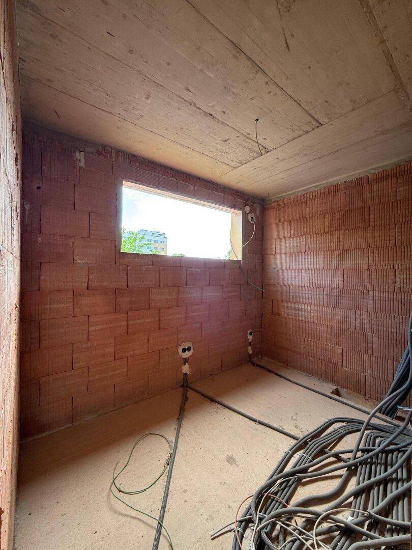 Unfertiges Zimmer im Rohbau mit einem Fenster und zahlreichen verlegten Kabeln.