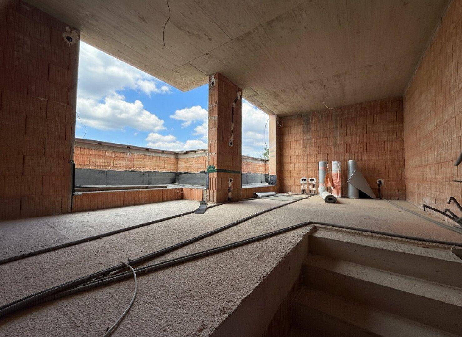 Großer Raum im Rohbau mit Zugang zu einer zukünftigen Terrasse und Blick in den Himmel.