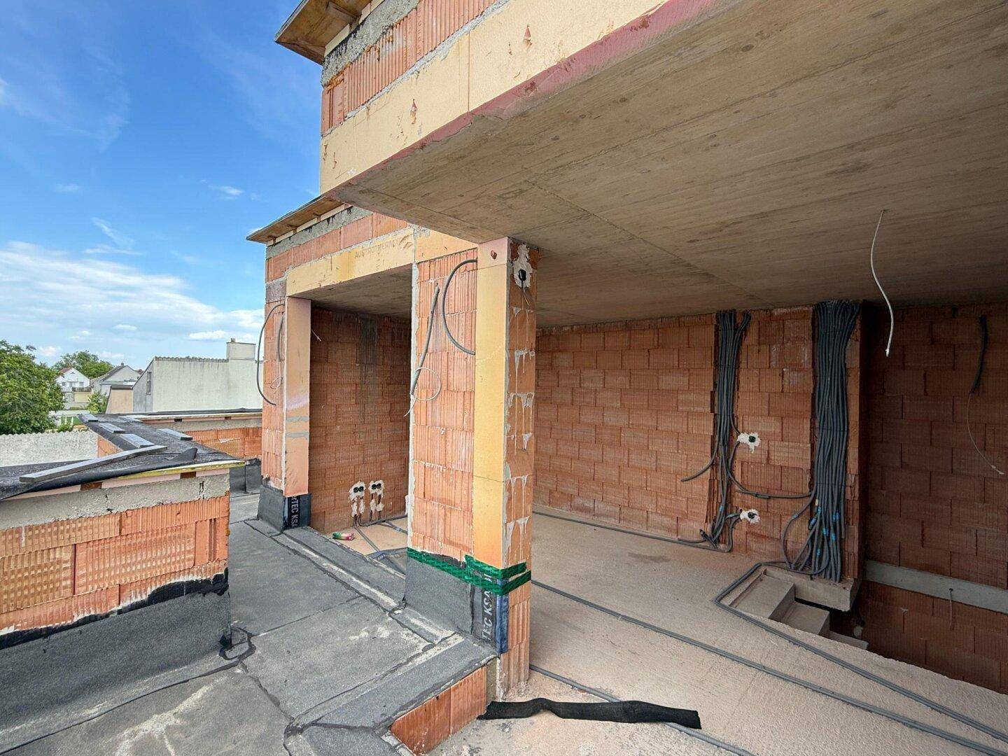 Innenraum im Rohbau mit Zugang zu einem Außenbereich und sichtbaren Installationen.