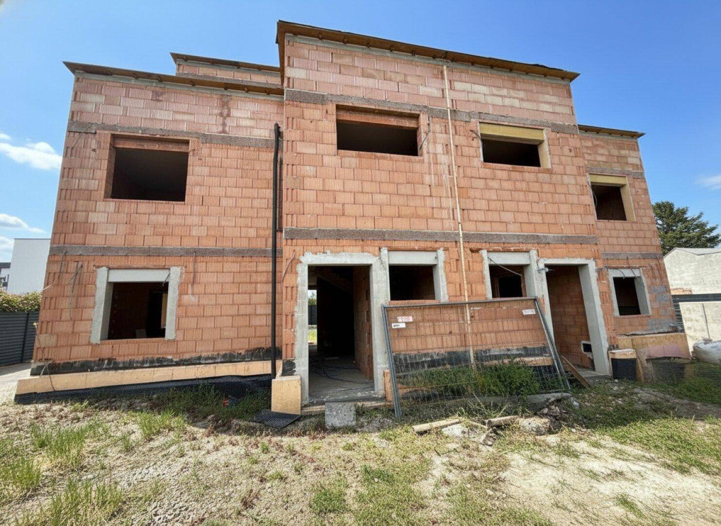 Vorderansicht des Rohbaus mit zukünftigen Fenster- und Türausschnitten und Bauzaun.