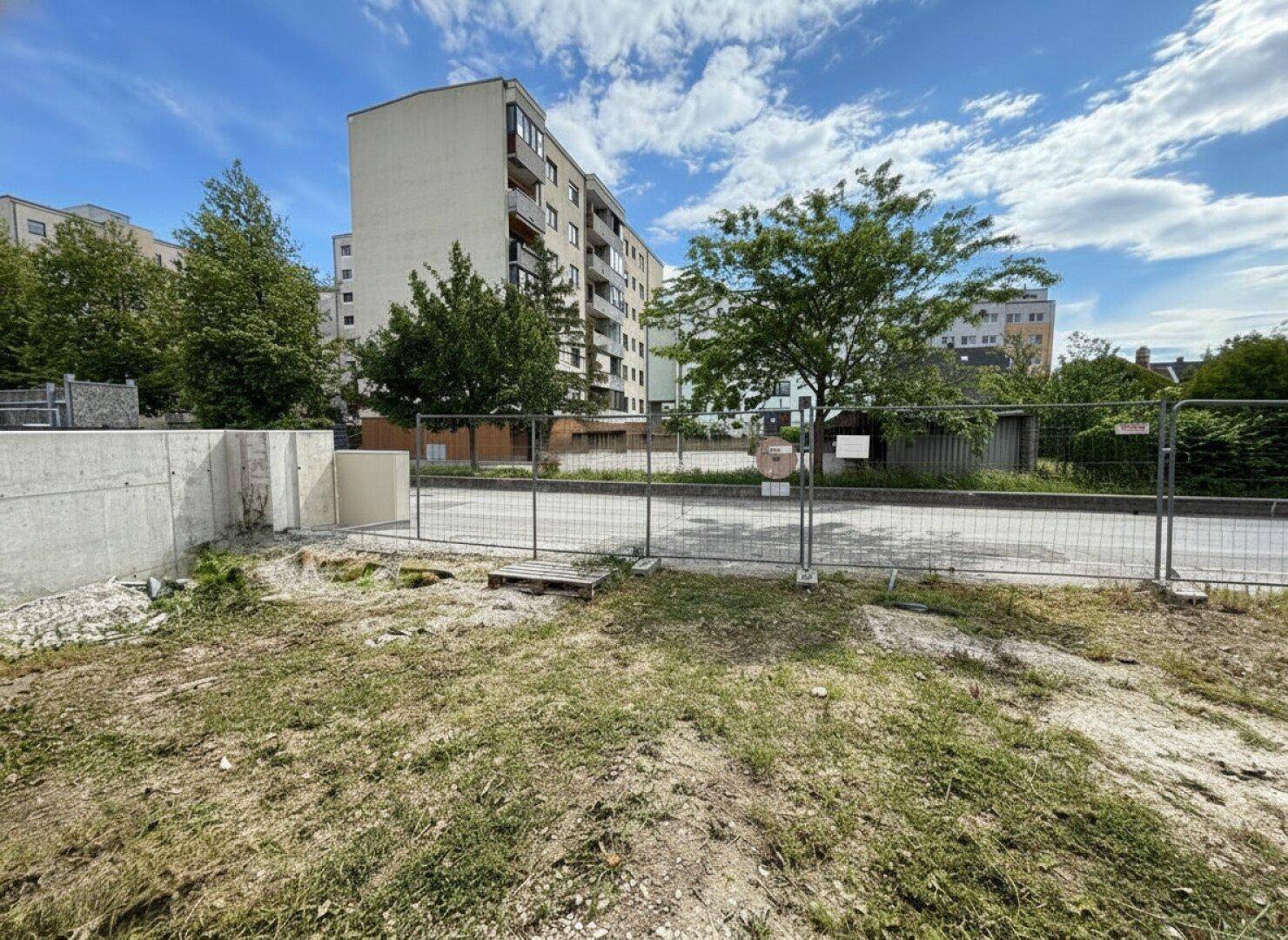 Baustelle mit Blick auf umliegende Mehrfamilienhäuser und eine provisorische Absperrung.