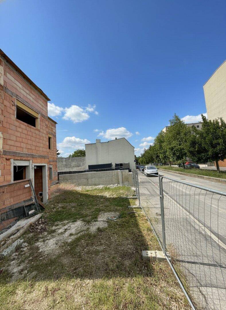 Seitenansicht der Baustelle mit angrenzender Straße und weiteren Gebäuden im Hintergrund.