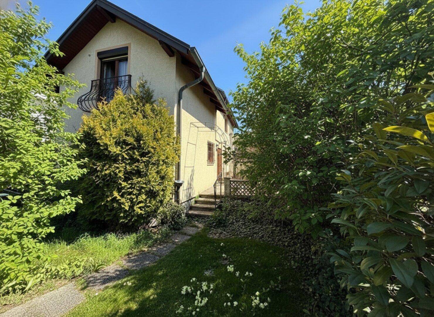 Ansicht des Hauses mit kleinem Balkon und gepflegtem Gartenbereich im Sonnenschein.