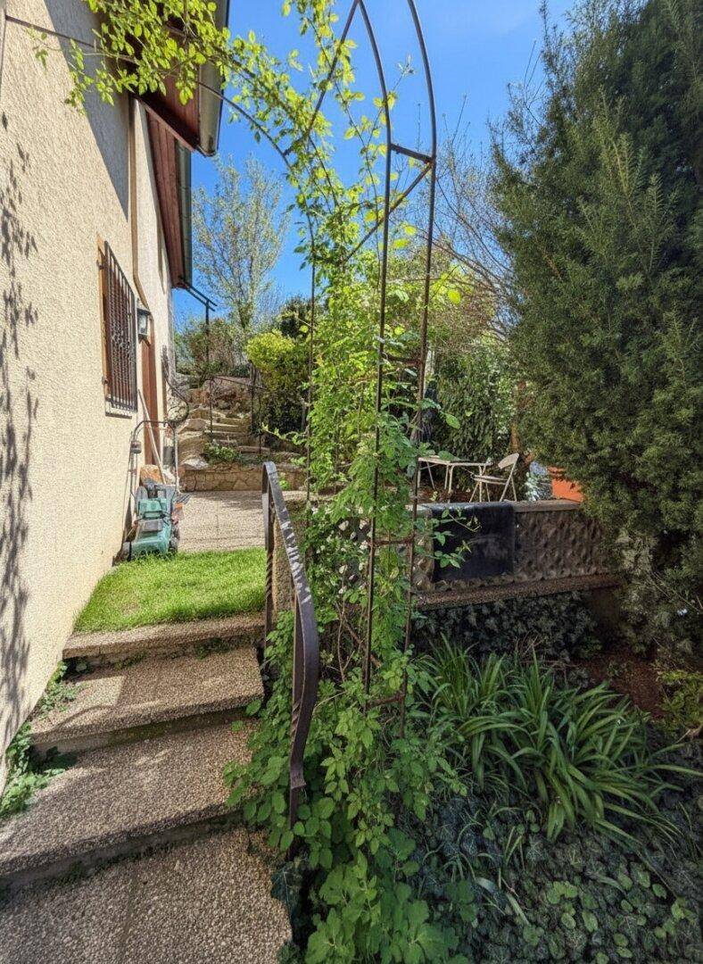 Steintreppe führt entlang der Hauswand zu einer kleinen Terrasse mit Gartenmöbeln.