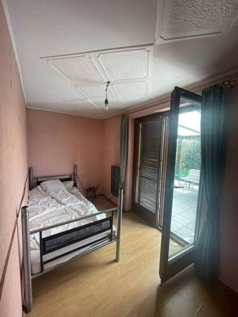 Schlafzimmer mit Zugang zu einer Terrasse, Holzboden und einfacher Einrichtung.