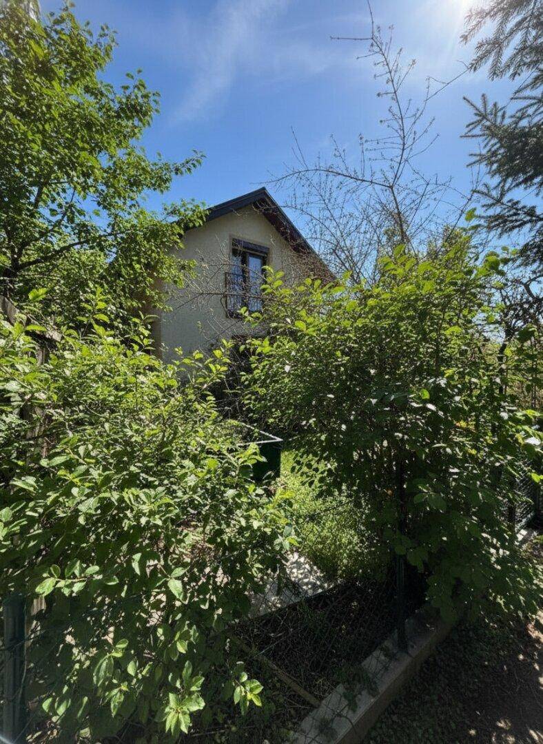 Das Haus ist umgeben von üppigem Grün und hohen Bäumen unter blauem Himmel.