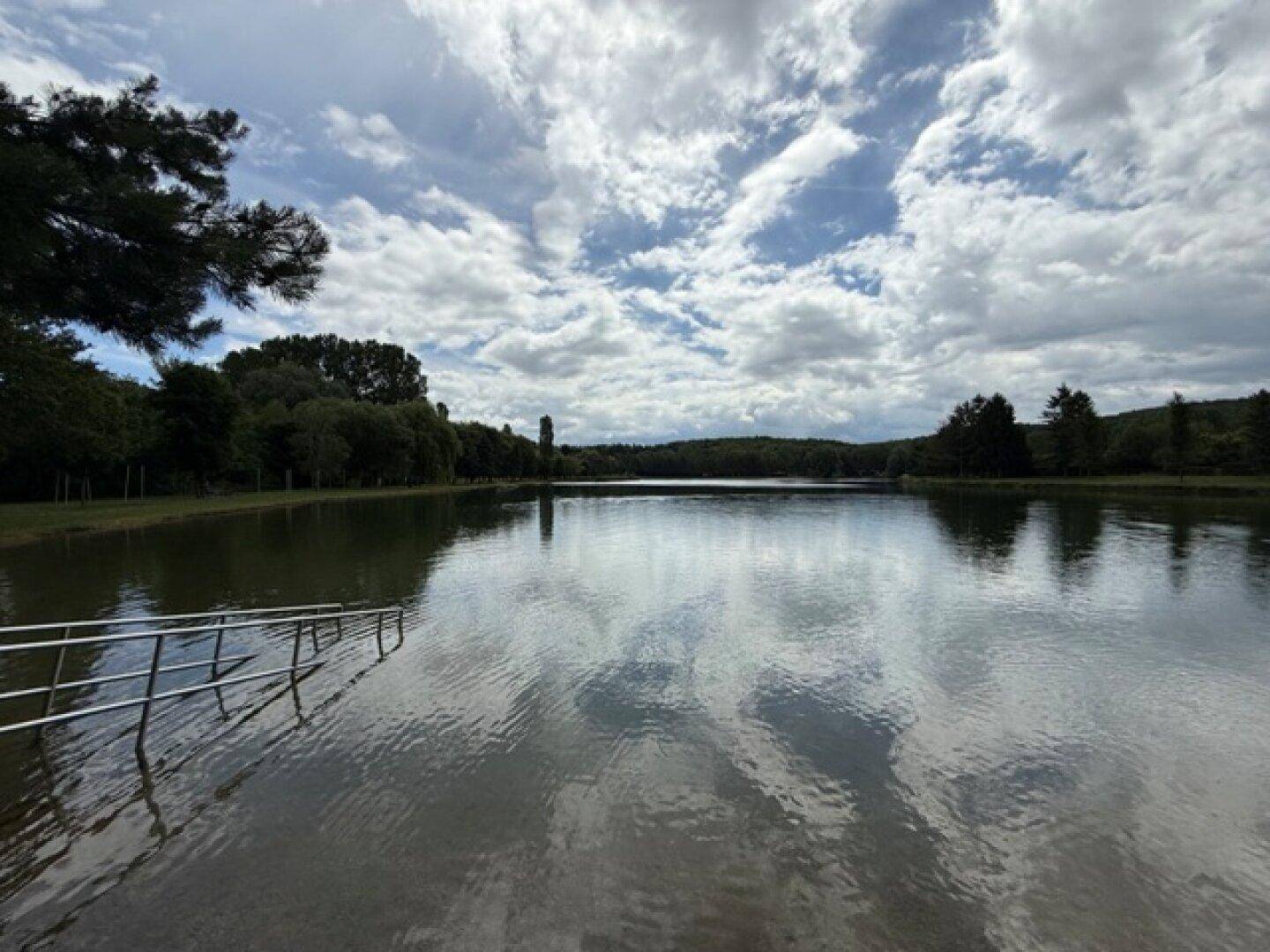 Weitläufiger See mit klarem Wasser und einem Einstieg, umgeben von grünen Ufern.