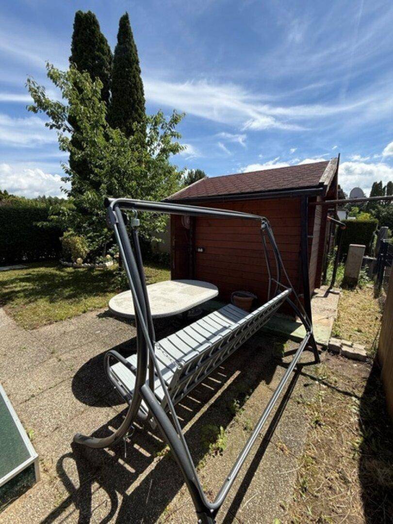 Gartenbereich mit Holzgartenhaus, Steintisch und einer Hollywoodschaukel.