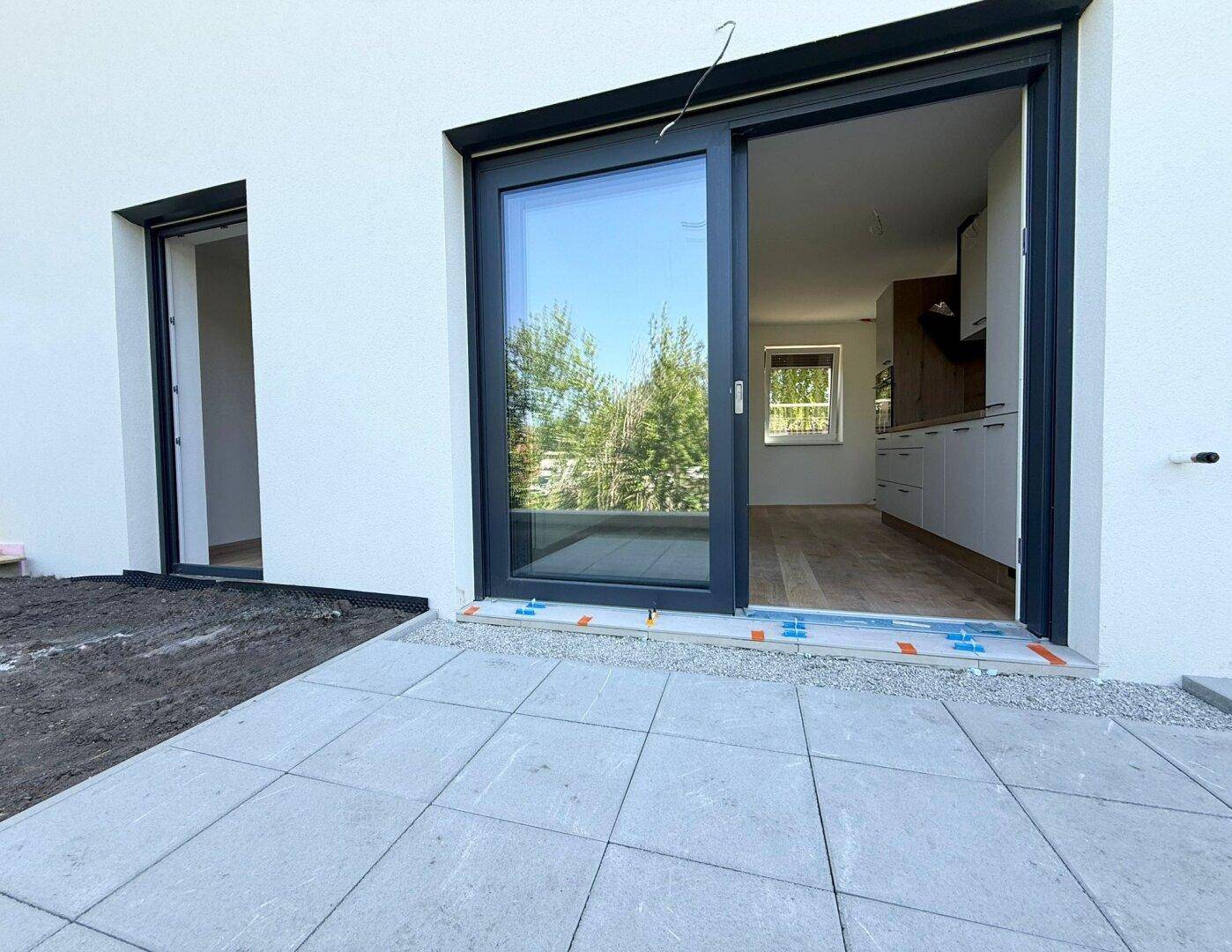 Große Schiebetür führt von der Küche auf eine neu gepflasterte Terrasse mit Blick ins Grüne.