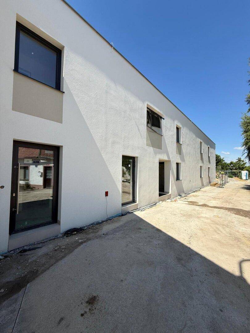 Lange Fassade eines modernen Neubaus mit mehreren Fenstern und Türen, umgeben von Baustellenbereich.
