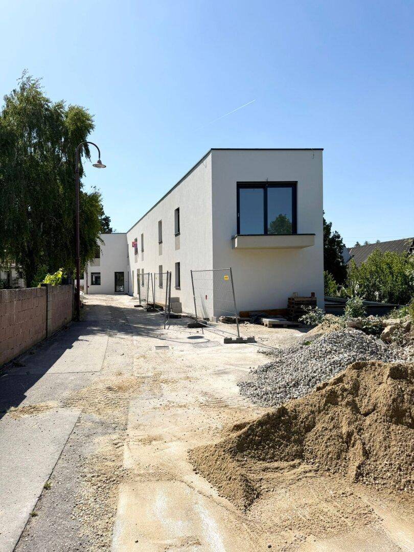 Moderner Neubau mit klaren Linien und großen Fenstern, umgeben von Baustellenmaterialien und einem Zaun.