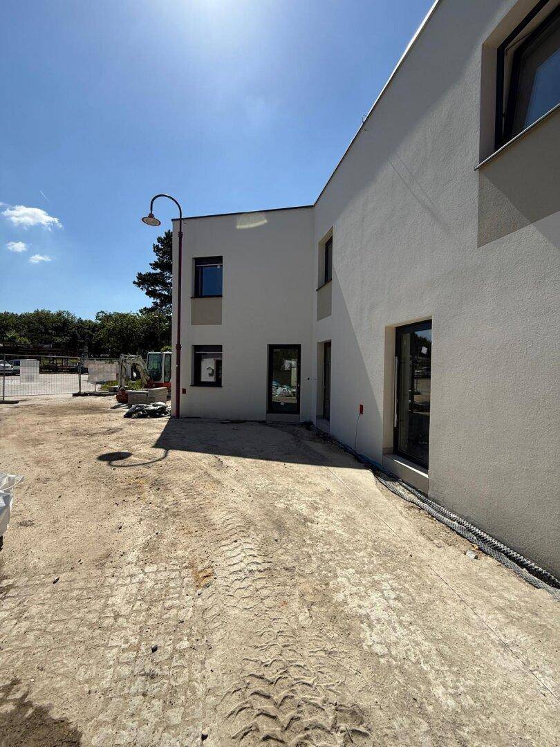 Seitenansicht eines modernen Neubaus mit schlichter Fassade und einem unfertigen Außenbereich.
