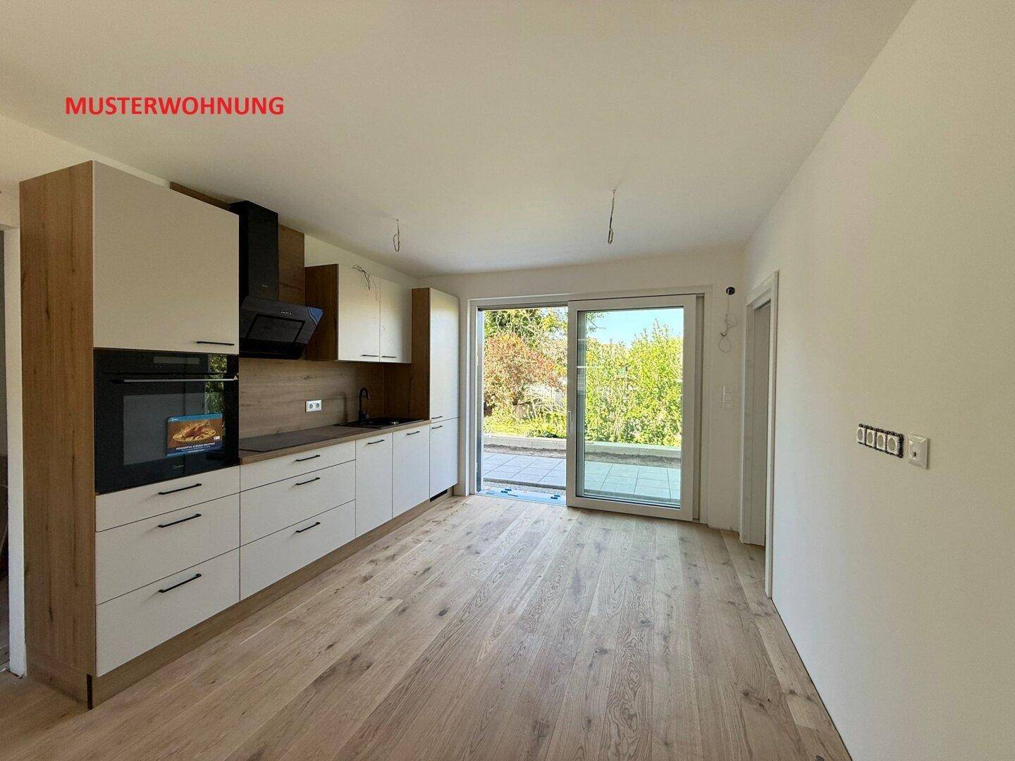 Moderne Einbauküche in einer Musterwohnung mit Holzboden und Zugang zur Terrasse mit Gartenblick.