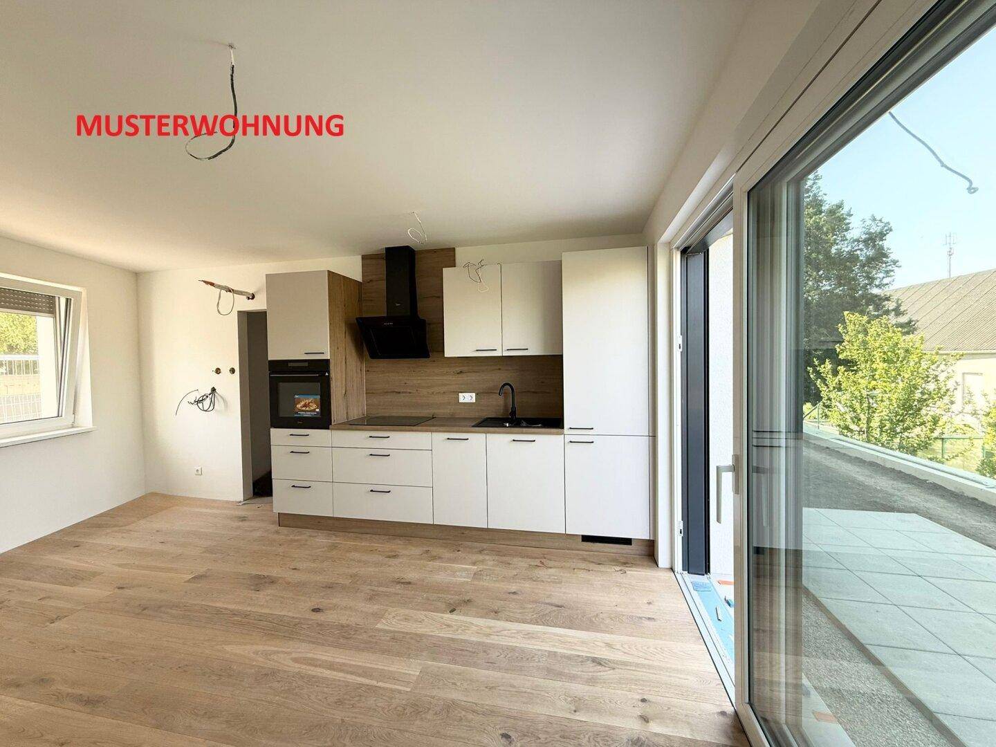 Helle Musterwohnung mit moderner Küche, Holzboden und großem Schiebefenster zur Terrasse.
