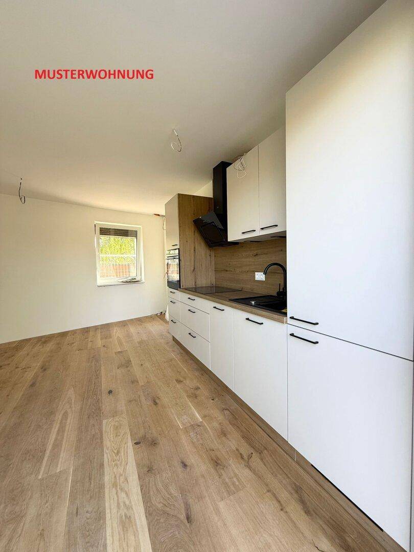 Stilvolle Musterküche mit weißen und holzfarbenen Schränken, dunkler Arbeitsplatte und Holzboden.