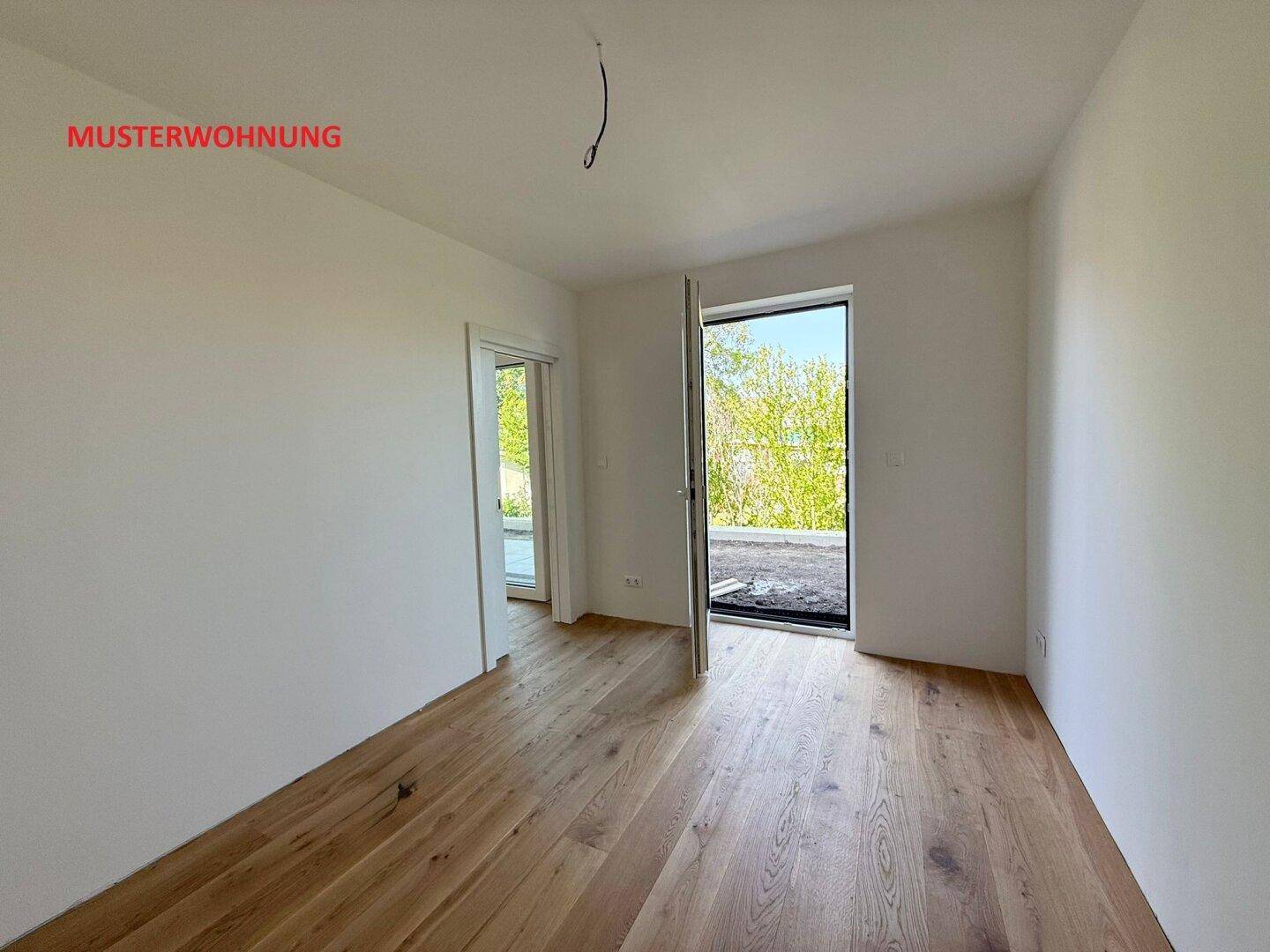 Heller Raum in einer Musterwohnung mit Holzboden und Zugang zu einem Außenbereich.