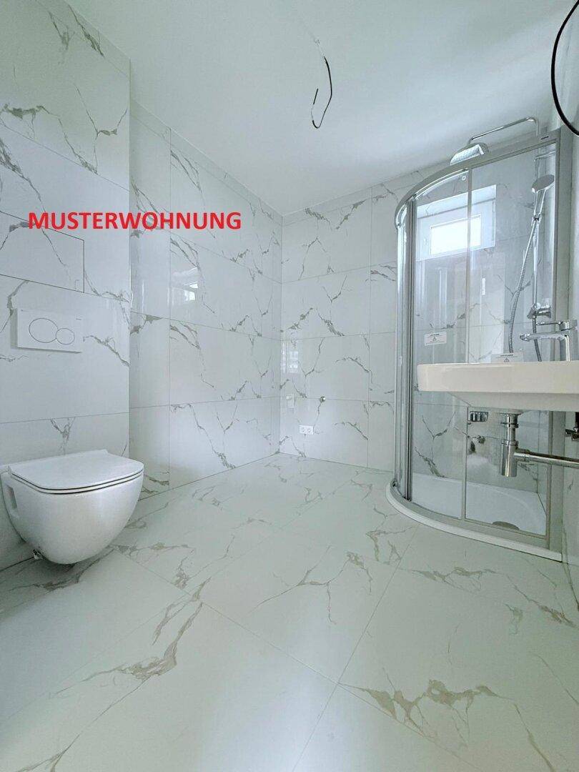 Helles Badezimmer in einer Musterwohnung mit modernen Marmorfliesen, Dusche und wandhängendem WC.