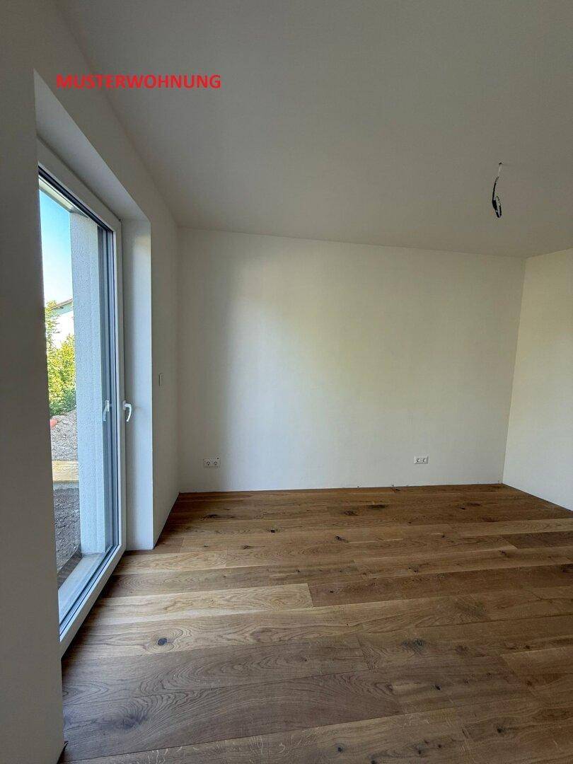 Lichtdurchfluteter Raum in einer Musterwohnung mit Holzboden und großem Fenster.