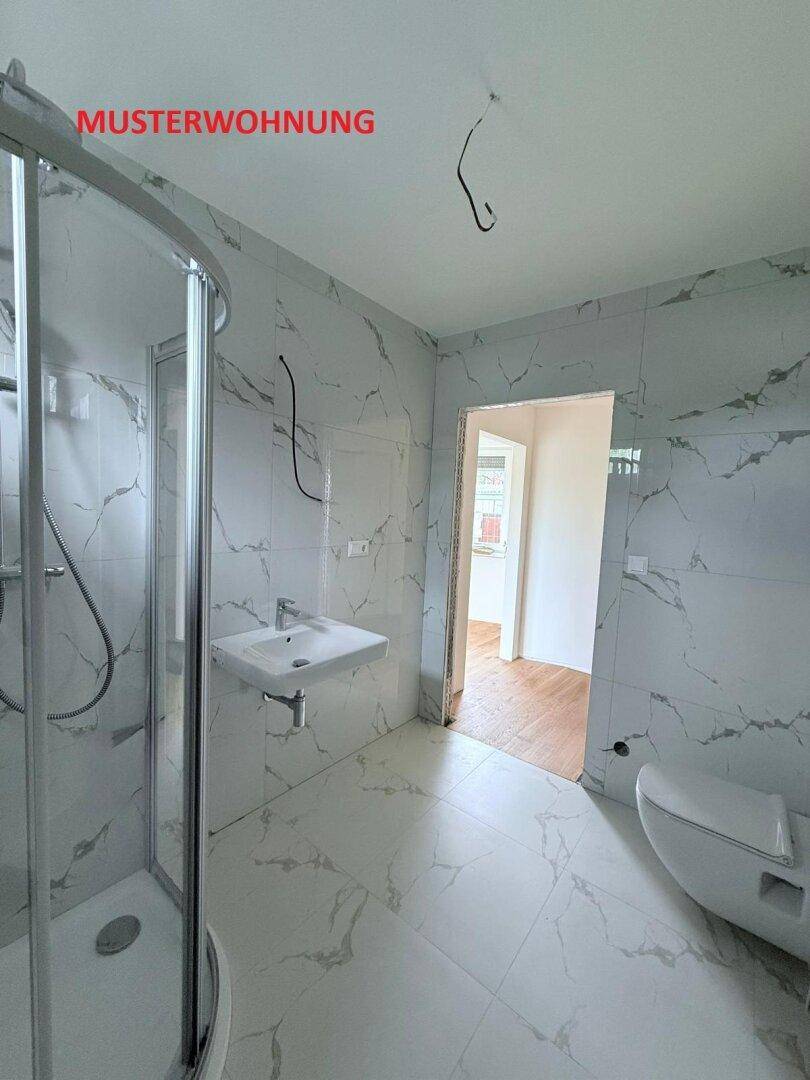 Modernes Badezimmer in einer Musterwohnung mit eleganten Marmorfliesen, Dusche und wandhängendem WC.