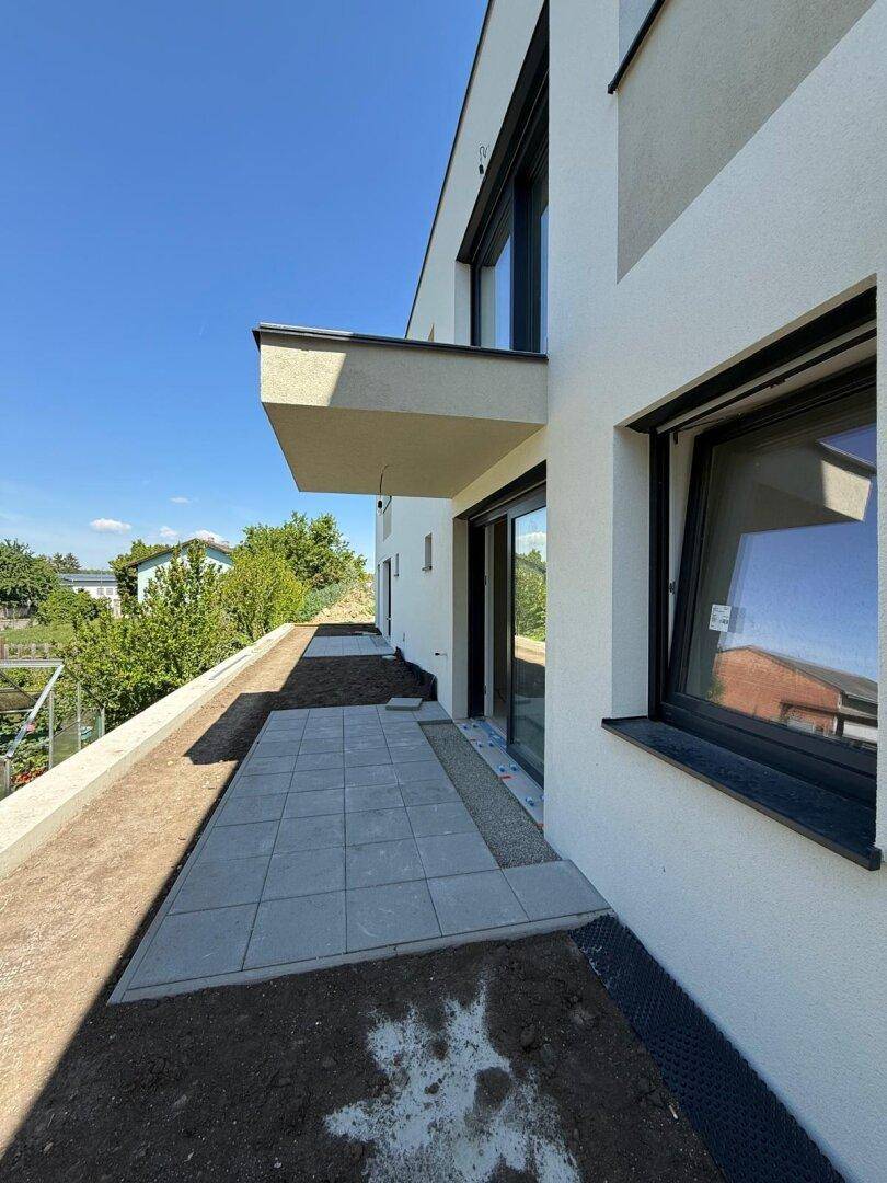 Moderne Gebäudefassade mit einer neu angelegten Terrasse und einem kleinen Balkon im oberen Stockwerk.