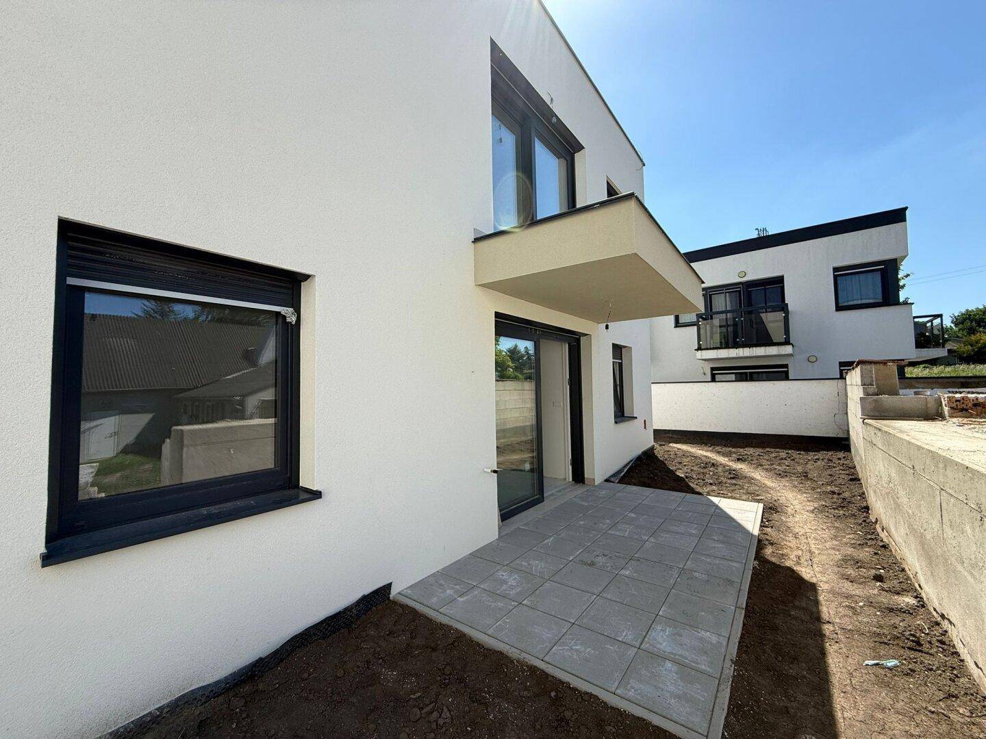 Moderne Neubauwohnung mit kleiner gepflasterter Terrasse und Zugang zum Gartenbereich.