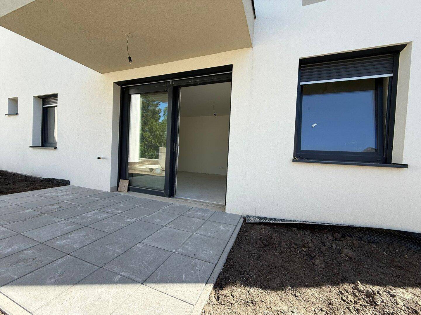 Nahaufnahme der gepflasterten Terrasse mit großer Schiebetür, die in den hellen Innenraum führt.
