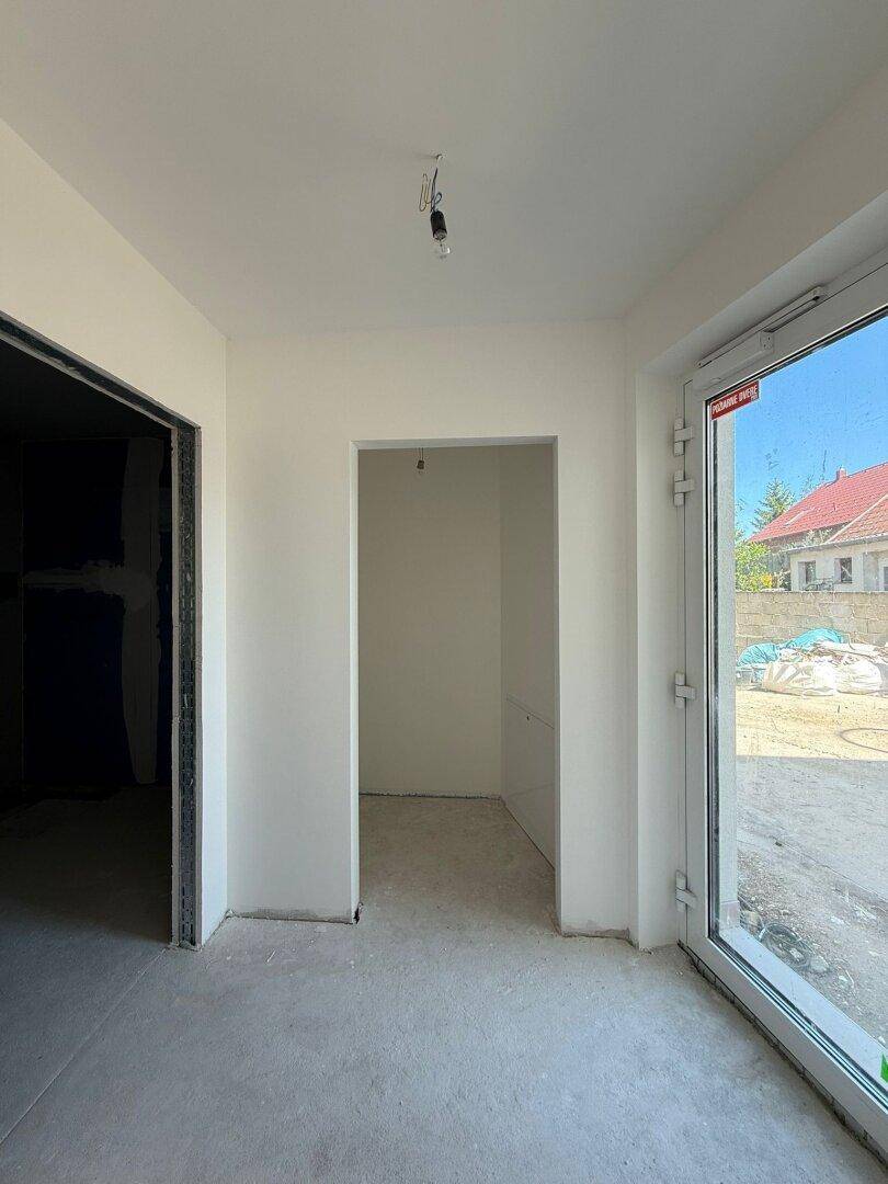 Heller Eingangsbereich im Rohbau mit Betonboden und einer großen Tür, die nach außen führt.