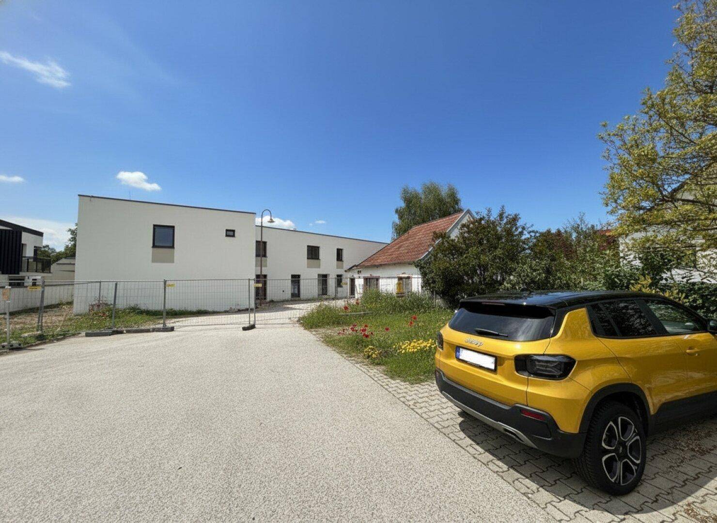 Außenansicht eines Neubaus mit moderner Architektur und einem gepflasterten Parkplatzbereich im Vordergrund.