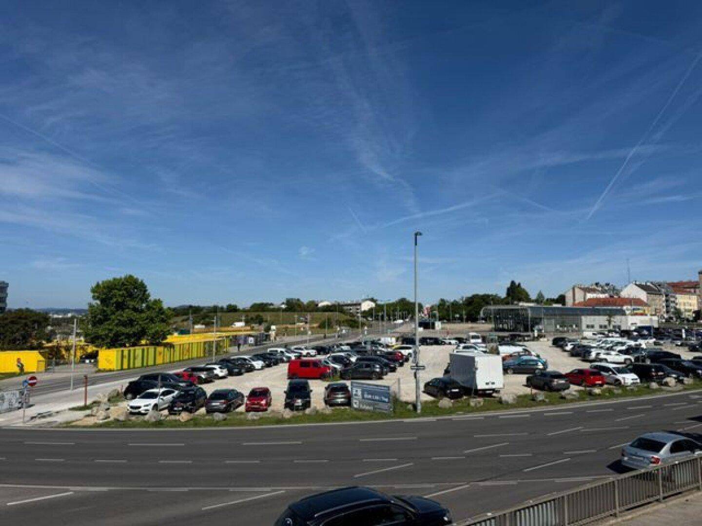 Großer Außenparkplatz mit zahlreichen Autos und umliegenden Straßen unter blauem Himmel.