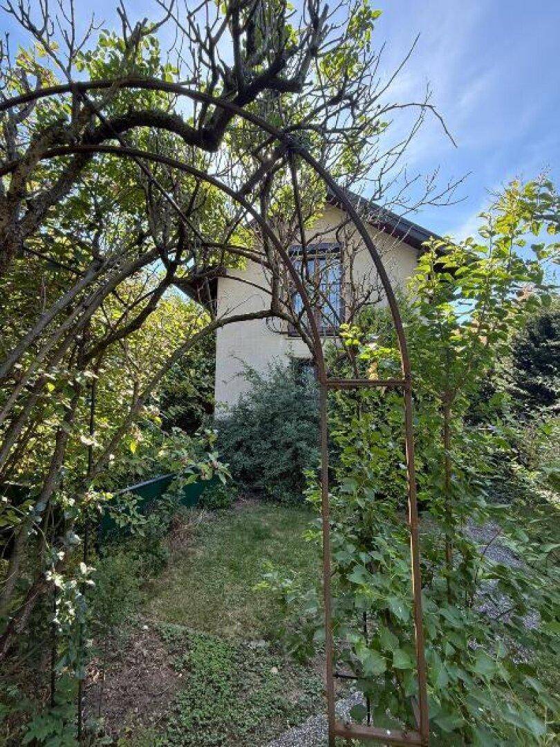 Gartenweg mit einem dekorativen Metallbogen führt zum Haus, umgeben von Bäumen und Sträuchern.