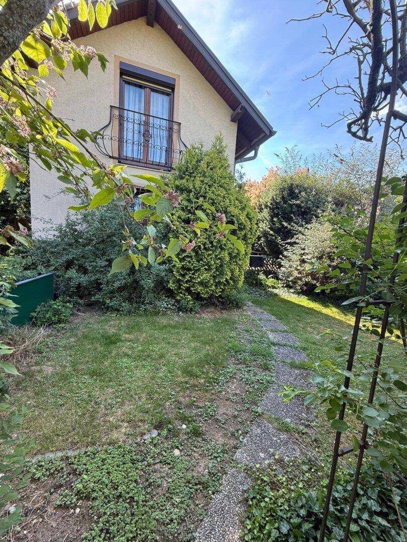 Grüner Gartenbereich mit einem Pfad und üppiger Vegetation neben dem Haus unter blauem Himmel.
