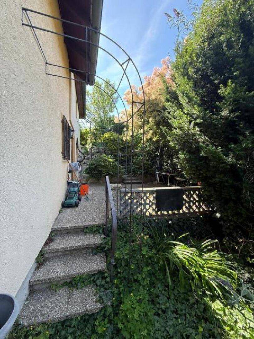 Steintreppe führt zu einem gepflasterten Bereich neben dem Haus, umgeben von viel Grün.