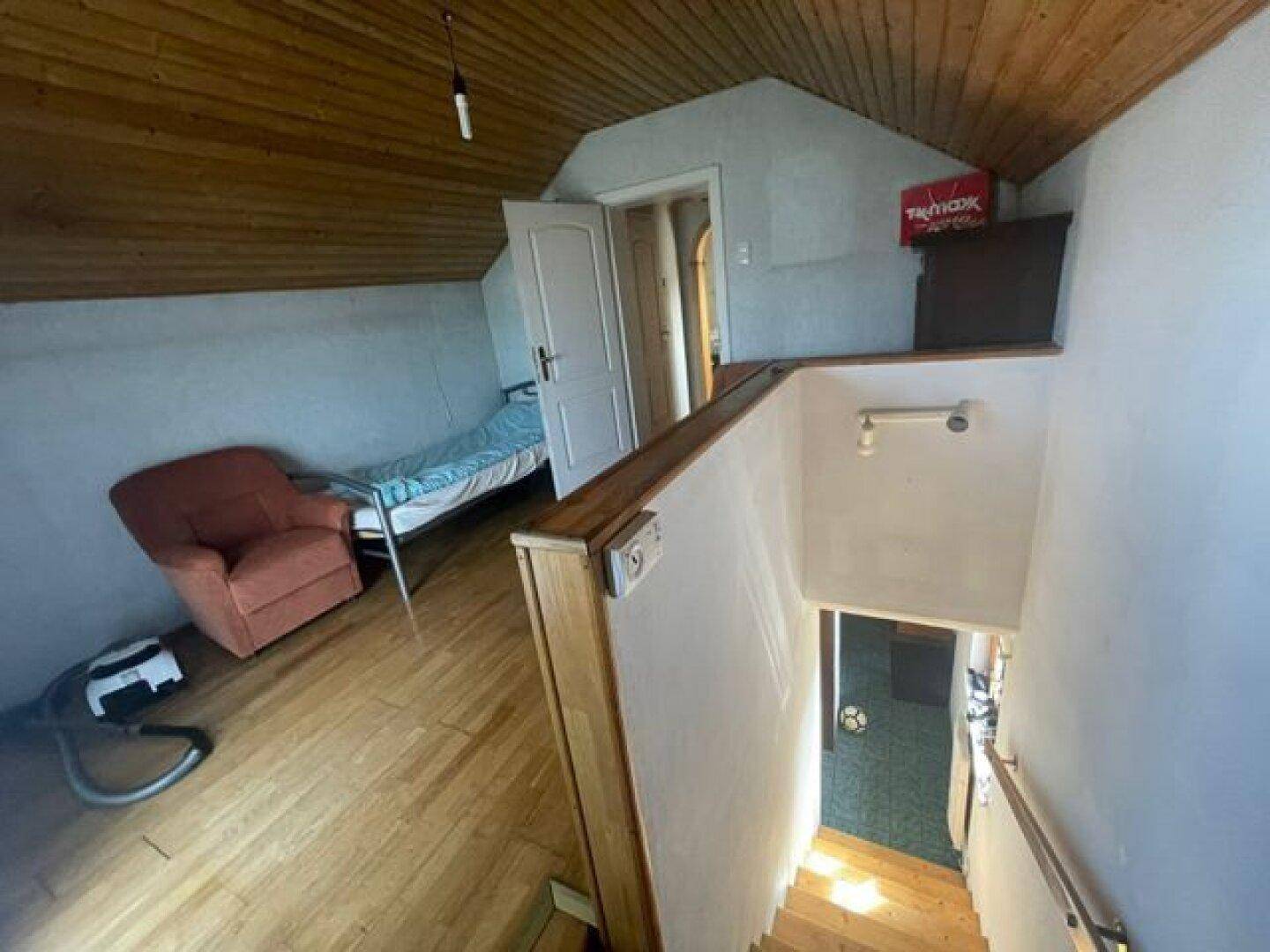 Dachgeschossbereich mit Holzboden, schrägen Wänden und einer Treppe, die nach unten führt.