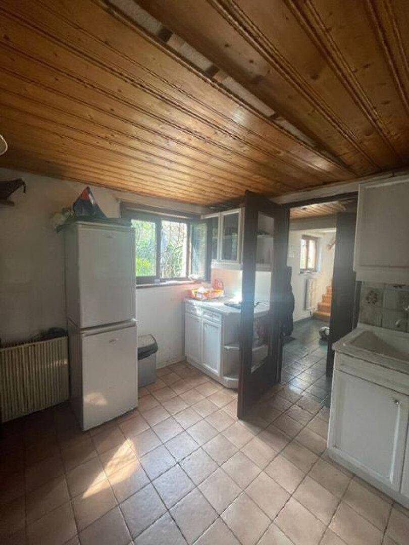 Funktionale Küche mit Fliesenboden, Holzbalkendecke und einem Fenster mit Blick ins Grüne.