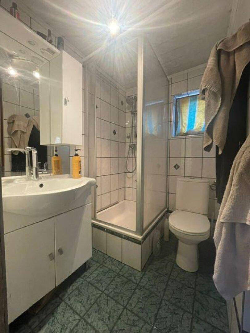 Gefliestes Badezimmer mit Duschkabine, Waschbecken und Spiegelschrank, hell beleuchtet.