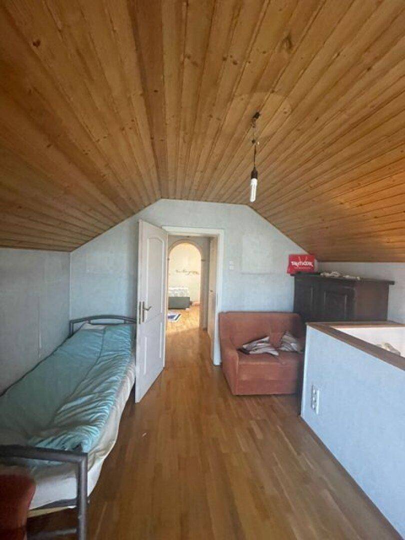 Dachgeschosszimmer mit Holzboden, Holzbalkendecke und einem Bett, hell und funktional.